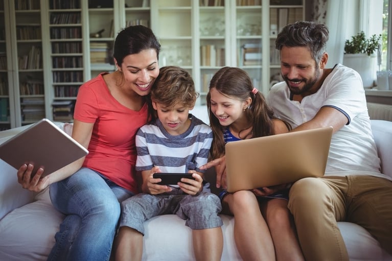  Happy family sitting on sofa and using laptop, mobile phone and digital tablet at home